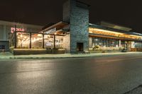 an outside restaurant lit up with a clock on the front of it in the dark