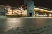 an outside restaurant lit up with a clock on the front of it in the dark