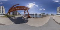 an orange bridge in a city near the water and building complex as seen in fish eye