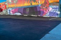 a mural with a rainbow - painted picture and tree in the background sits at the end of a parking lot