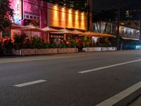 a city road and sidewalk filled with tables and chairs at night with bright lights on the buildings