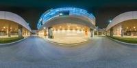 a panoramic photo of a curved street at night with cars and people around the perimeter