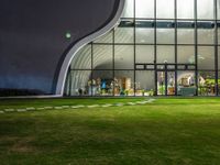 a glass building with a lawn and walkways between two buildings at night that have the lights on and the reflection in the window