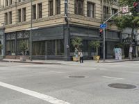 people crossing the street at a cross walk under traffic lights, in front of a brown building