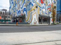 a person standing on the side of a street next to a building with brightly colored walls