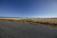 the empty road near a wooden fence on a sunny day with a few clouds in the distance