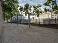 a bench that is by a fence in the sidewalk looking at a river and buildings