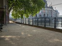 a bench that is by a fence in the sidewalk looking at a river and buildings