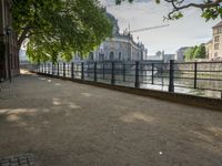 a bench that is by a fence in the sidewalk looking at a river and buildings