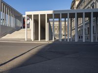 the large, empty sidewalk with multiple columns in front of the building with two signs