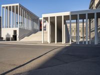 the large, empty sidewalk with multiple columns in front of the building with two signs