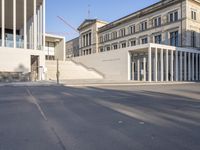 the large, empty sidewalk with multiple columns in front of the building with two signs