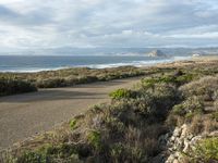 a view of the coast from the hillside on a cloudy day and two people with surfboards