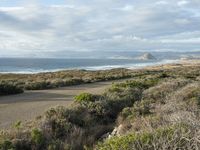 a view of the coast from the hillside on a cloudy day and two people with surfboards