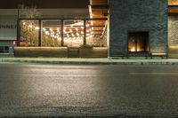 a store front with lights on the outside window at night, next to the street