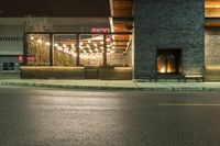 a store front with lights on the outside window at night, next to the street