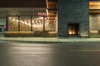 a store front with lights on the outside window at night, next to the street