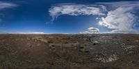 an image taken in an fish eye lens of clouds and a volcanic mountain with sparse dirt