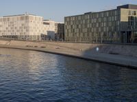 the people are walking along the side of the canal in the water near some buildings