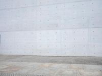 a man walking on a sidewalk past a concrete wall and a brick walkway with an iron gate