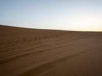 a lone person on a desert walking with a dog in hand with the sun setting behind them