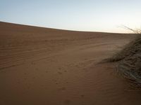 a lone person on a desert walking with a dog in hand with the sun setting behind them