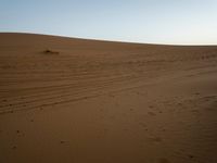 a lone person on a desert walking with a dog in hand with the sun setting behind them