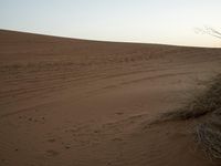 a lone person on a desert walking with a dog in hand with the sun setting behind them