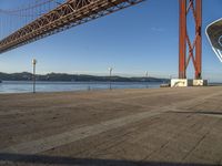 a person walking towards the bay while standing under a bridge over water and with mountains in the distance