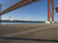 a person walking towards the bay while standing under a bridge over water and with mountains in the distance