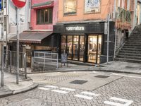 street with stores and signs and stairs up to them, and a pedestrian on the sidewalk