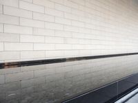 a water feature reflecting light and sky in the center of a white brick wall with a black edge