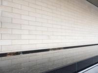 a water feature reflecting light and sky in the center of a white brick wall with a black edge