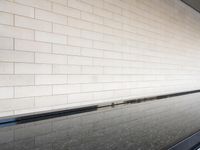 a water feature reflecting light and sky in the center of a white brick wall with a black edge