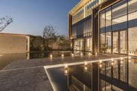 a view of a house at dusk with glass walls and a pool in the foreground