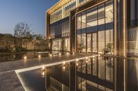 a view of a house at dusk with glass walls and a pool in the foreground