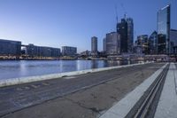 a bench with no people on it by the water in front of tall buildings near water