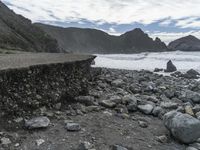 the waves are breaking near the concrete retaining with rocks in front of them and cliffs in the distance