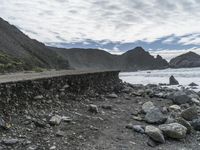 the waves are breaking near the concrete retaining with rocks in front of them and cliffs in the distance