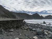 the waves are breaking near the concrete retaining with rocks in front of them and cliffs in the distance