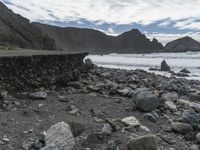 the waves are breaking near the concrete retaining with rocks in front of them and cliffs in the distance