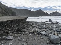 the waves are breaking near the concrete retaining with rocks in front of them and cliffs in the distance