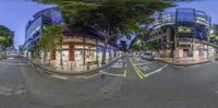 this fisheye photo shows the intersection of a city street at night, with trees on either side of the street and buildings behind