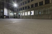 an empty parking lot at night with the sun on top of a building in the background