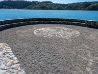 a circular stone walkway near the ocean surrounded by mountains and trees by the water's edge