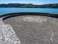 a circular stone walkway near the ocean surrounded by mountains and trees by the water's edge