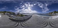 a wooden bridge going over a bay with houses and clouds in the background and a small building behind