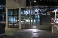 the lights are on at the entrance to a building with many windows and steps in it