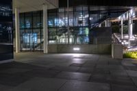 the lights are on at the entrance to a building with many windows and steps in it