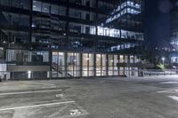 an empty parking lot in front of a building at night with buildings behind it and stairs